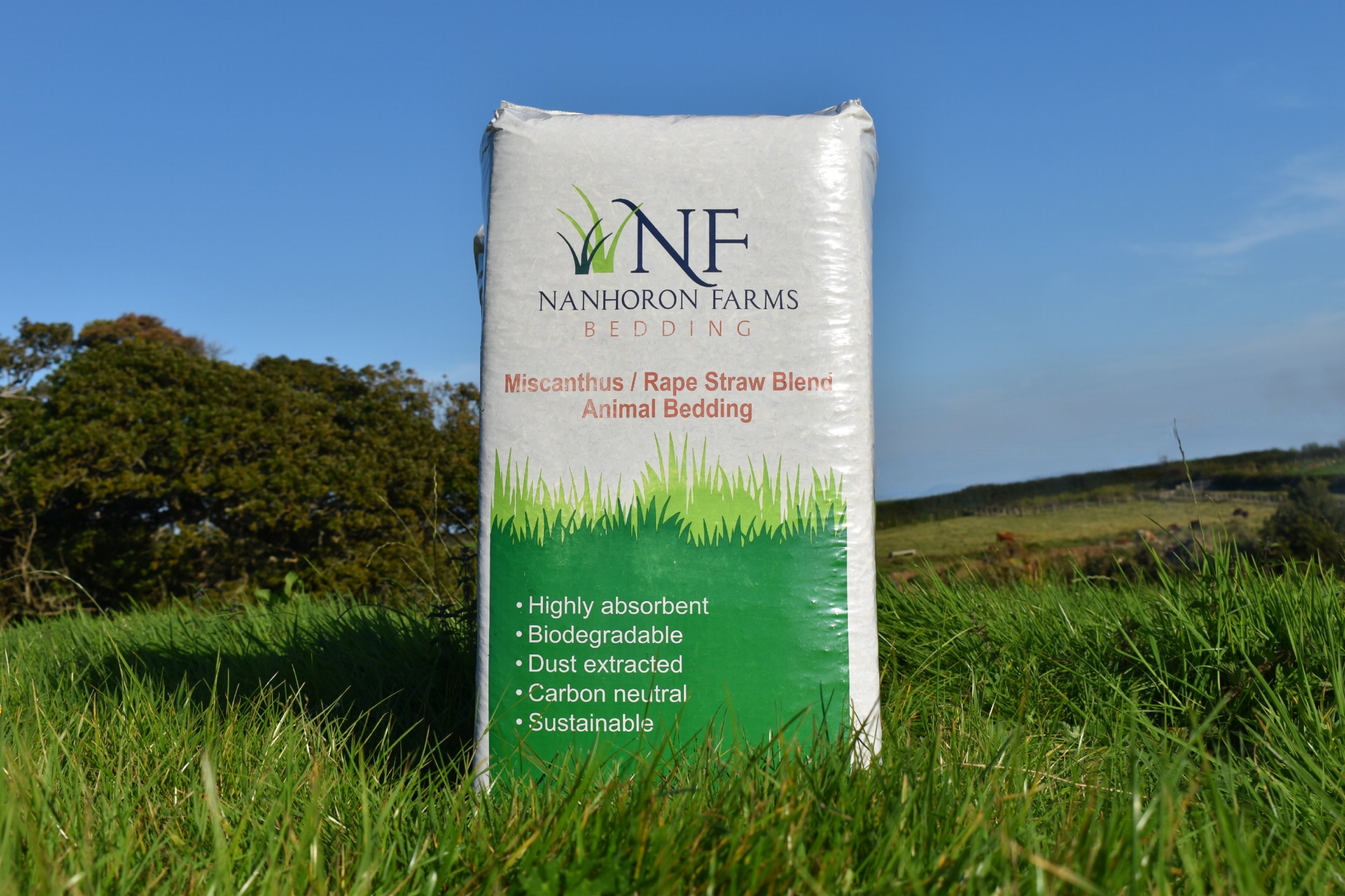 Bag of Nanhoron Farms animal bedding in a grassy field with trees and blue sky in the background